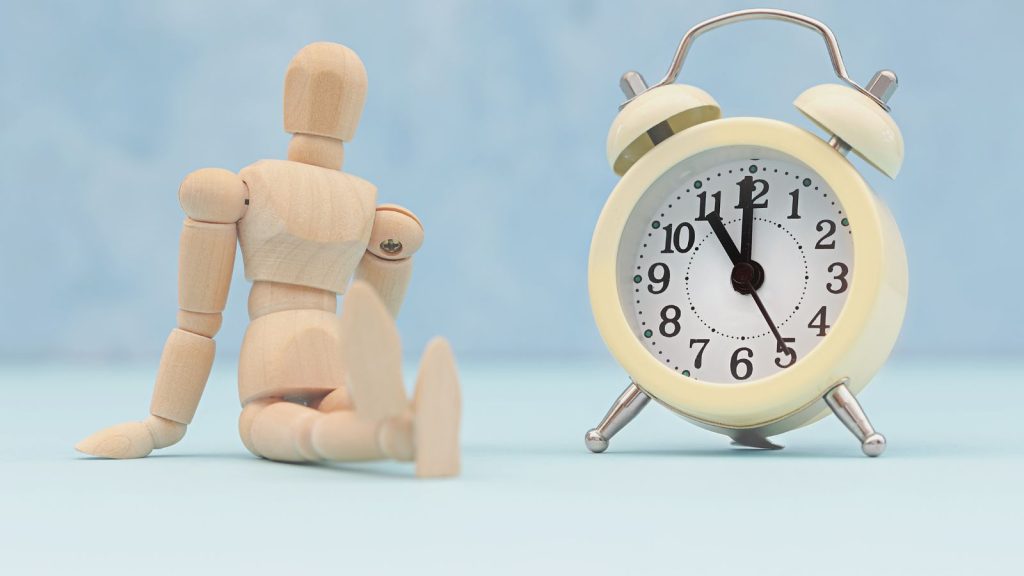 everyday procrastination. Image of toy human figure sitting and relaxing while an alarm clock shows its late night.